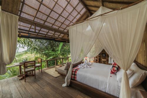 a bedroom with a bed and a table on a deck at LeLangit Eco Cabin in Sidemen