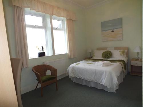 a bedroom with a bed and a chair and two windows at Taormina Guest House in Tenby