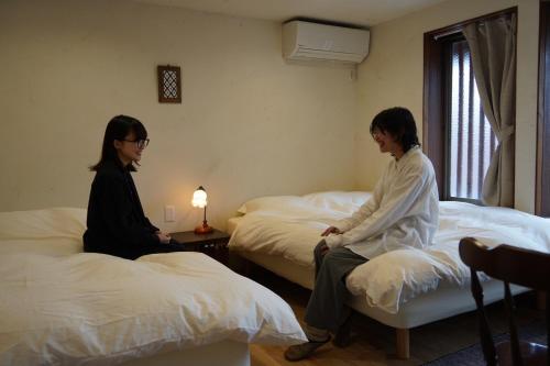 two women sitting on beds in a room at Masukichi -hostel,cafe,souvenir,guide- in Seto