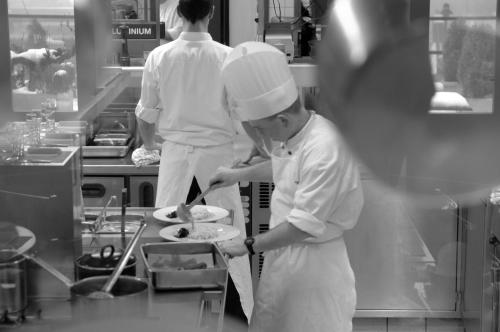 a couple of chefs in a kitchen preparing food at Hotel Leo Station, Villa et Annexes in Bastogne