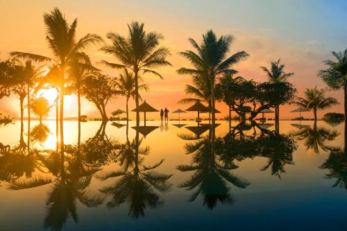 a resort pool with palm trees and the sunset at Ayodya Resort Bali in Nusa Dua