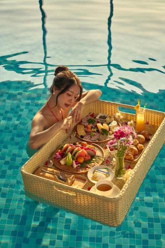 a woman in a pool with a tray of food in the water at DeLaSea Ha Long Hotel - Modern Bayview Escape in Ha Long