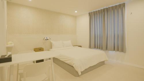 a white bedroom with a bed and a window at Jeju Stay Hotel in Jeju