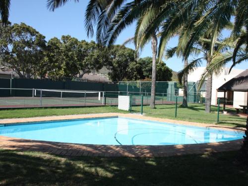 a swimming pool with a tennis court and palm trees at Amies Self-Catering Apartments in Panorama