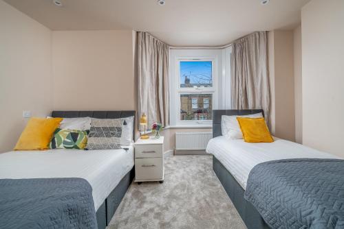 two beds in a small room with a window at Exquisite 4Bedroom House 4 Contractors & Large Families with Private Garden, Fully Equipped Kitchen and Close Proximity to Train & Bus Stations in Finchley
