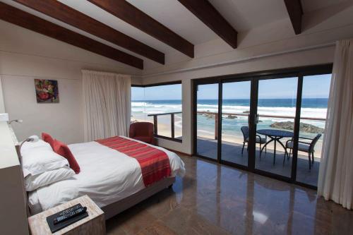 a bedroom with a bed and a balcony with the ocean at Archrock Resort in Plettenberg Bay
