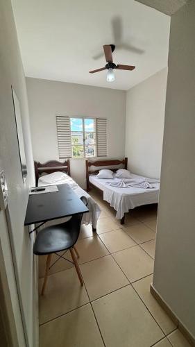 a room with two beds and a table and a ceiling fan at Hotel Olympia in Cláudio