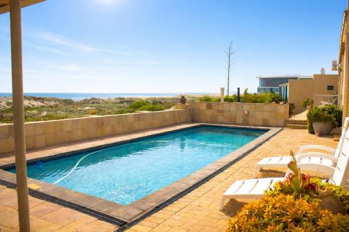 a swimming pool with chairs and the ocean in the background at 14 Penguin Place, Melkbosstrand in Melkbosstrand