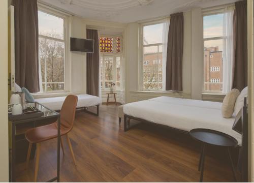 a bedroom with two beds and a desk and windows at Quentin Canal House Hotel in Amsterdam