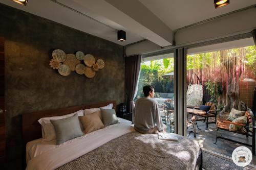 a man sitting on a bed in a bedroom with a patio at Lannatika Villa in Chiang Mai