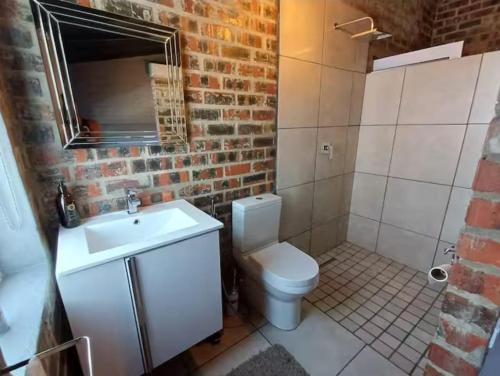 a bathroom with a white toilet and a brick wall at Luxurious and spacious 2 level apartment in Tygerberg Hills