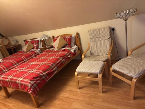 a bed with a red plaid blanket and two chairs at Squirrel View Cottage B&B in Buckenham