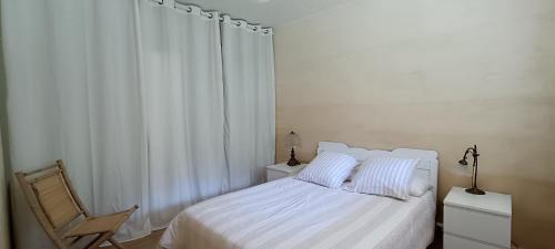 a white bedroom with a bed and a chair at Le Village Champignon in Aspet