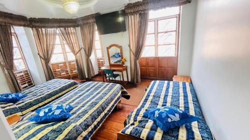 two beds in a room with two windows at Hotel Plaza del Teatro in Quito
