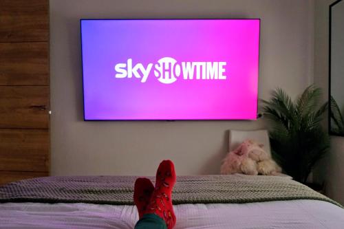 a person with red shoes sitting on a bed with a tv at Casa Belice Huelva in Huelva