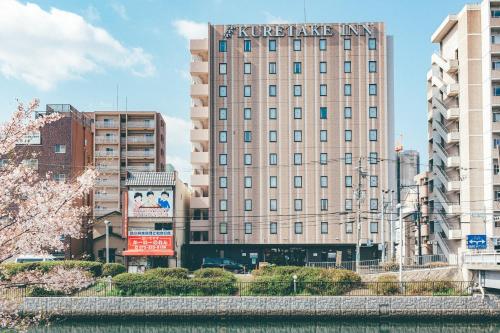 a tall building with a sign on it next to a river at Kuretake Inn Nankai Sakai-Ekimae in Sakai