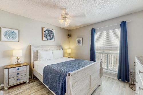 a bedroom with a bed and a window with blue curtains at Beach Club: The Lighthouse in Padre Island