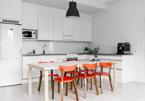 a white kitchen with orange chairs and a white table at Modern Two-Bedroom Apartment with Sauna & Free Parking in Turku