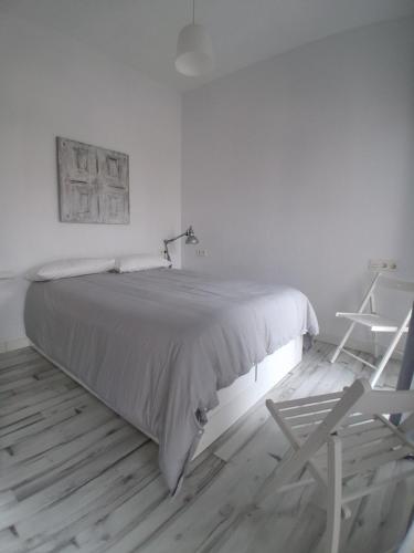 a white bedroom with a bed and a chair at San Atón apartamentos in Badajoz