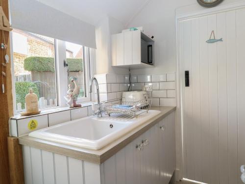 a white kitchen with a sink and a window at Herbies Cottage in Snettisham