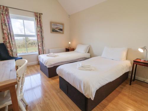a bedroom with two beds and a table and a window at Derg Cottage in Strabane