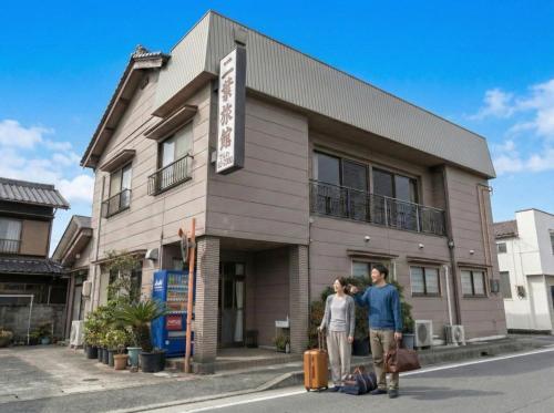 two people with luggage standing in front of a building at Tabist Futaba Ryokan Tatsuno in Tatsuno