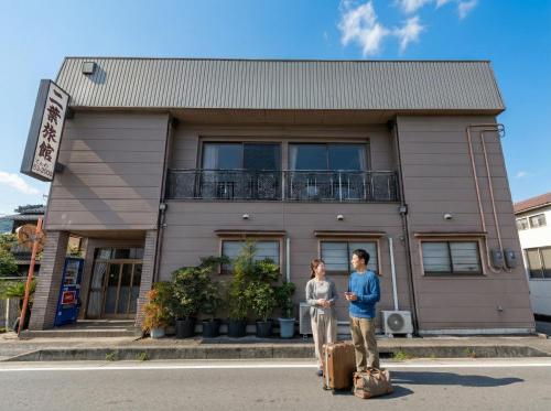 two people standing in front of a building with luggage at Tabist Futaba Ryokan Tatsuno in Tatsuno