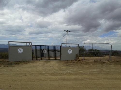 a gate in a dirt field with a cloudy sky at Natures Rest Lapa in Oudtshoorn