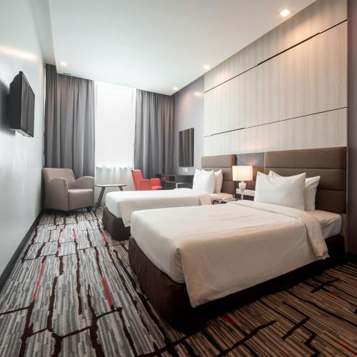 a hotel room with two beds and a chair at Promenade Hotel Bintulu in Bintulu
