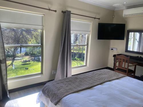 a bedroom with a bed and two windows and a television at Riverfront Golf Estate House in Parys