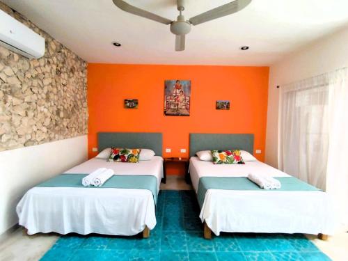 two beds in a room with orange walls at Casa colonial tranquila cerca del centro, Casa Solecito in Valladolid