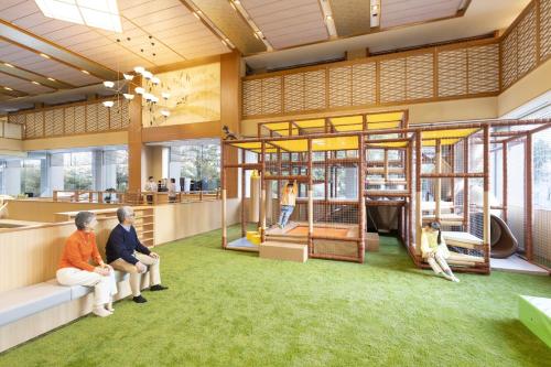 two people sitting on a bench in a building with a playground at Ooedo Onsen Monogatari Premium Seiunkaku in Awara