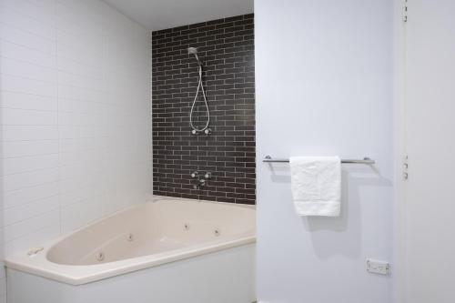 a white bathroom with a tub and a black tile wall at Bay View - The Trio in Lorne
