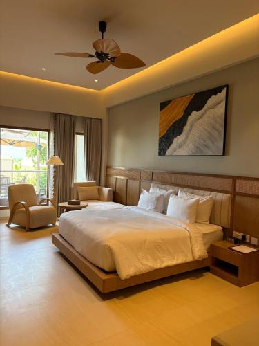 a bedroom with a bed and a chair and a ceiling fan at Peninsula Del Mar Beach Resort in Udupi