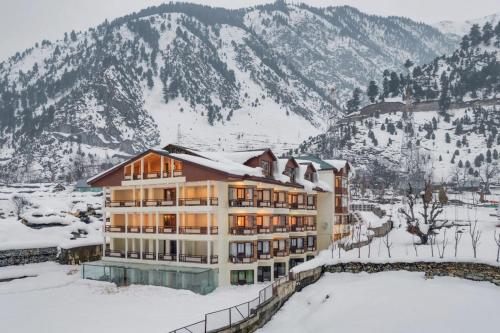 a building in the snow with mountains in the background at Badar Resorts & Spa by Stay Pattern Riverside in Sonāmarg
