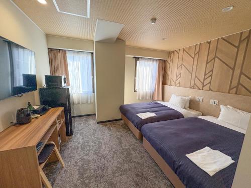 a hotel room with two beds and a desk at Hotel Livemax Budget Kagoshima Tenmonkan in Kagoshima