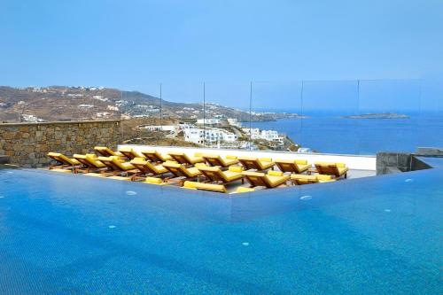 a pool with yellow chairs and a view of the ocean at Myconian Korali Relais & Chateaux in Mýkonos City
