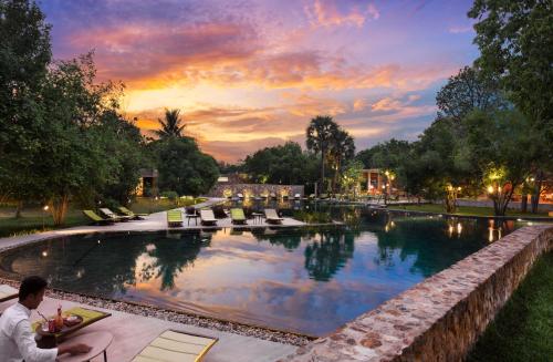 a man sitting next to a swimming pool at sunset at Templation Hotel in Siem Reap