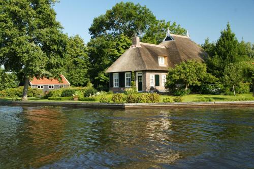 une maison au toit de chaume sur la rive d'une rivière dans l'établissement Hotel - Restaurant - Cafe- Geertien, à Blokzijl