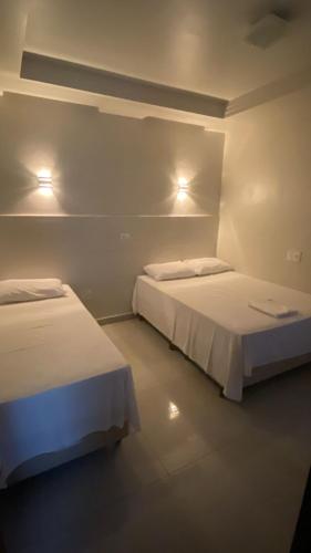 two beds in a room with lights on the wall at Hotel Acauã in Campo Mourão