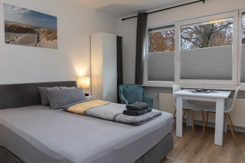 a bedroom with a bed and a desk and windows at Infinity Stay Apartmenthaus am Park in Wilhelmshaven
