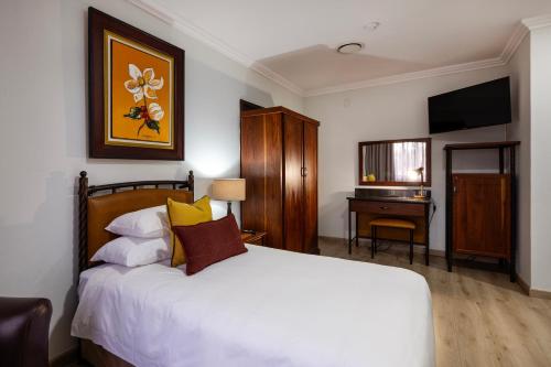 a bedroom with a bed and a desk with a television at Basdenwood Hotel in Centurion