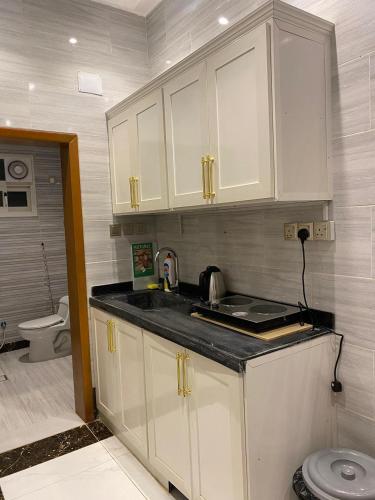 a kitchen with white cabinets and a sink and a toilet at كيان الين in Muhayil