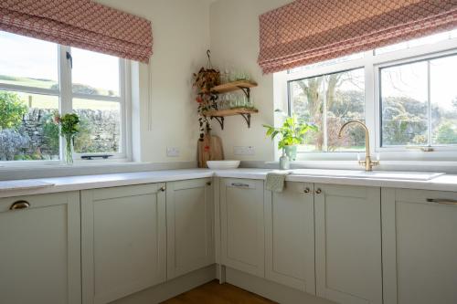 a kitchen with white cabinets and two windows at Skinnel Cottage in Kirkcudbright