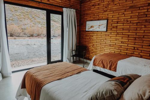 two beds in a room with a large window at Hosteria Manzano Amargo in Manzano Amargo