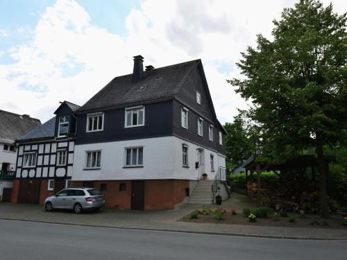 a white and black house with a car parked in front at Bright apartment in the Sauerland with conservatory large terrace and awning in Assinghausen
