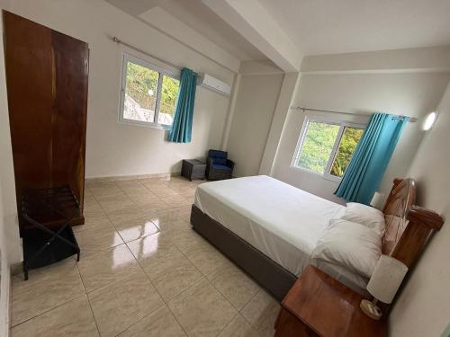 a bedroom with a bed and two windows with blue curtains at You 4 Ric Piton Suites in Soufrière
