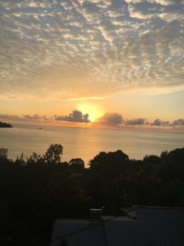 a sunset over a body of water with trees and clouds at Sunset View Self Catering in Anse Boileau