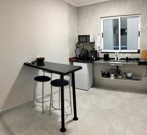 a kitchen with a table and two bar stools at Kitnet Moderna com Ar e Vaga Privativa Coberta in Votorantim