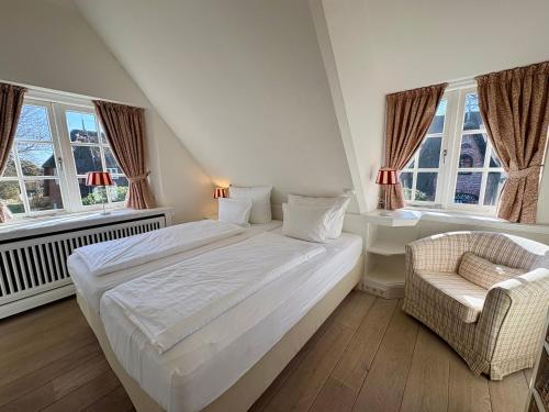 a bedroom with a bed and a chair and windows at Salig Hüs in Kampen